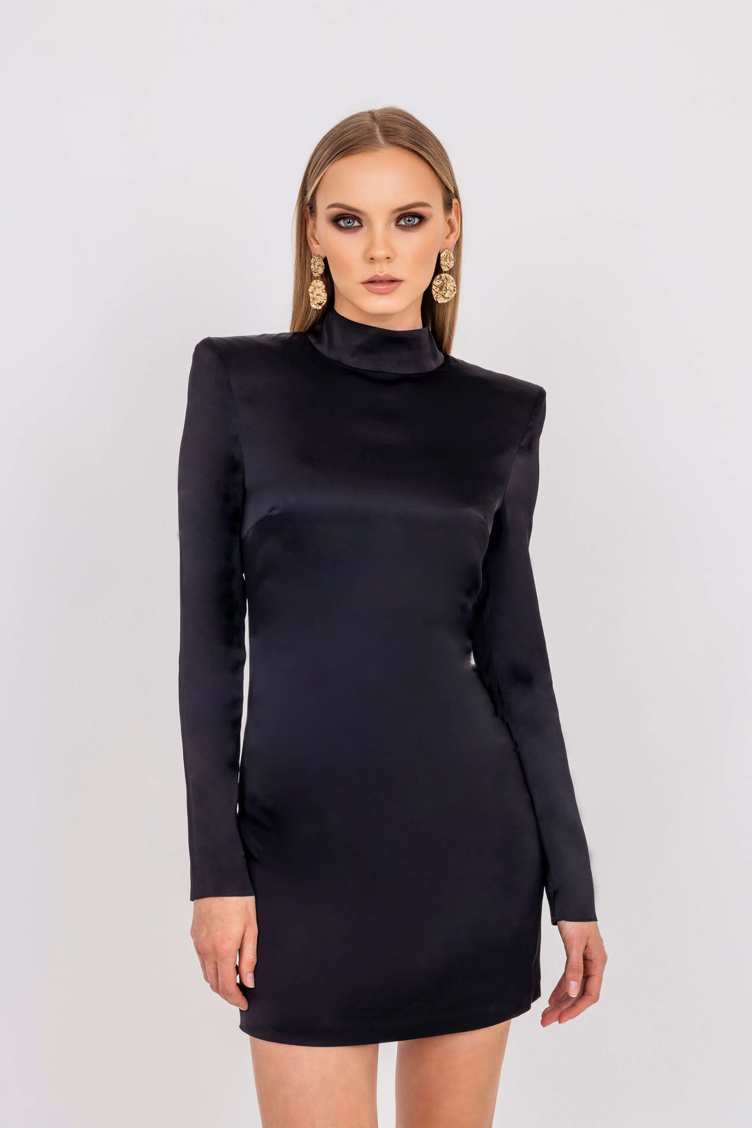 Leochèle Valentina Black Satin Long Sleeves mini dress - model standing in fitted black dress with gold earrings for Leochèle campaign look 3
