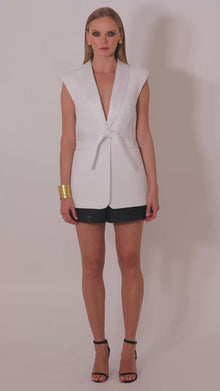 Model wearing the Roza white sleeveles  blazer with belt by Leochèle turns and walks out of frame